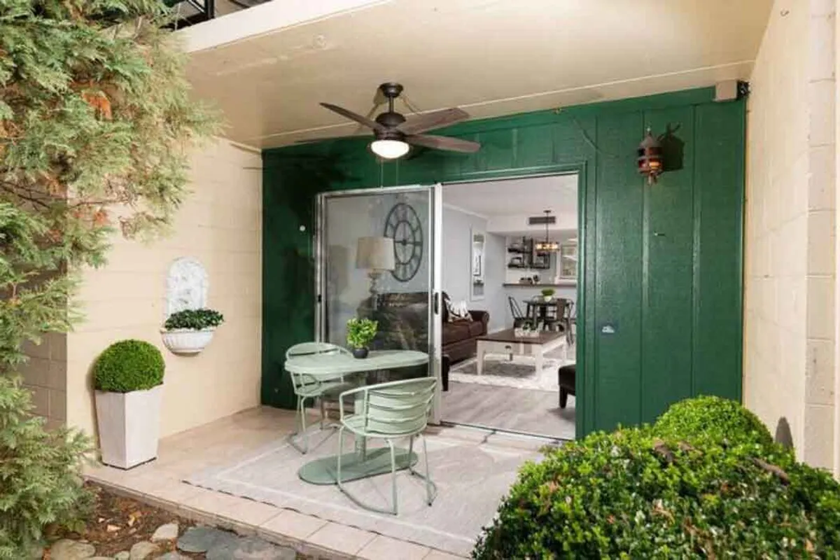 An outdoor seating area framed by a green wall, potted plants, and a sliding glass door leading into the building. The space is ideal for relaxing with coffee, reading, or entertaining, and hints at the seamless transition between the outdoors and interior comfort.
