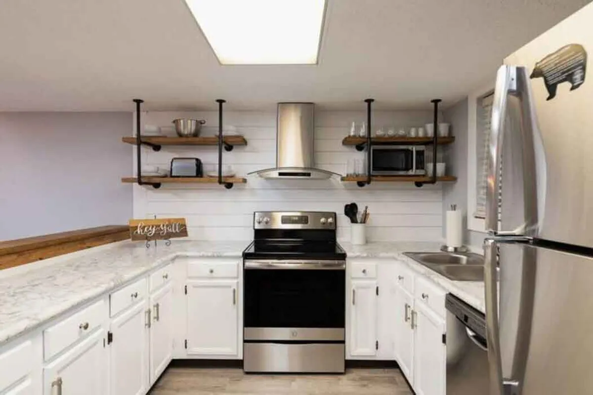 The kitchen is highlighted by sleek stainless steel appliances, expansive marble countertops, and open shelving. The inviting setup encourages both casual cooking and entertaining, with ample space and a contemporary design.