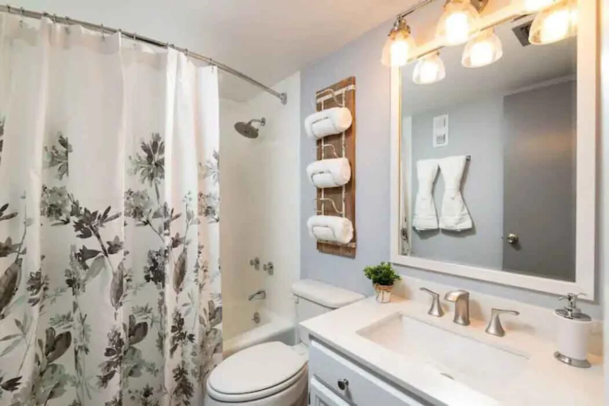 A bright, modern bathroom with a floral shower curtain, sleek vanity, illuminated mirror, and fresh towels on a rack. The space feels fresh, inviting, and perfect for relaxing routines.