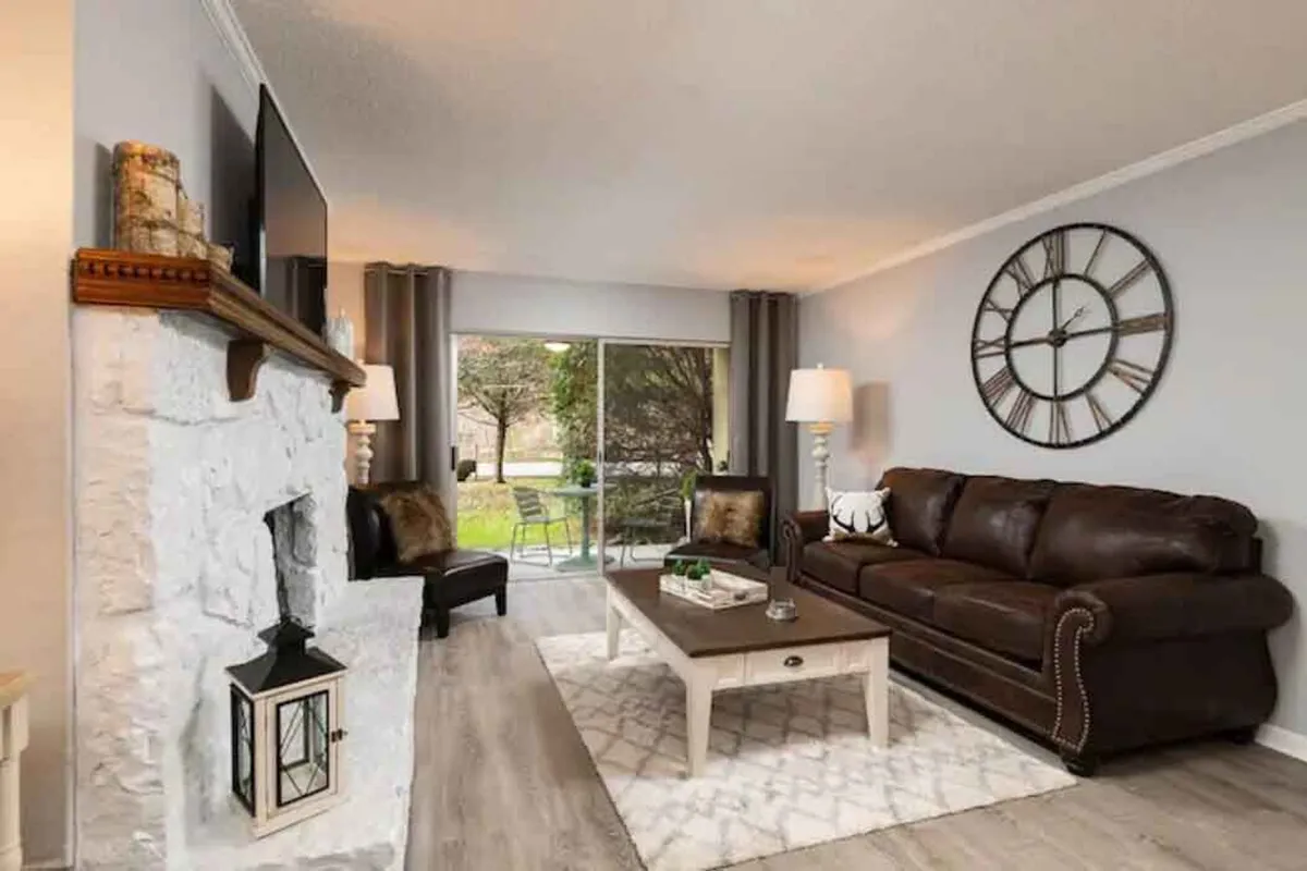 A living area with a rich brown leather couch, a large wall clock, a warm fireplace, and a coffee table, all set in a cozy, intimate ambiance.